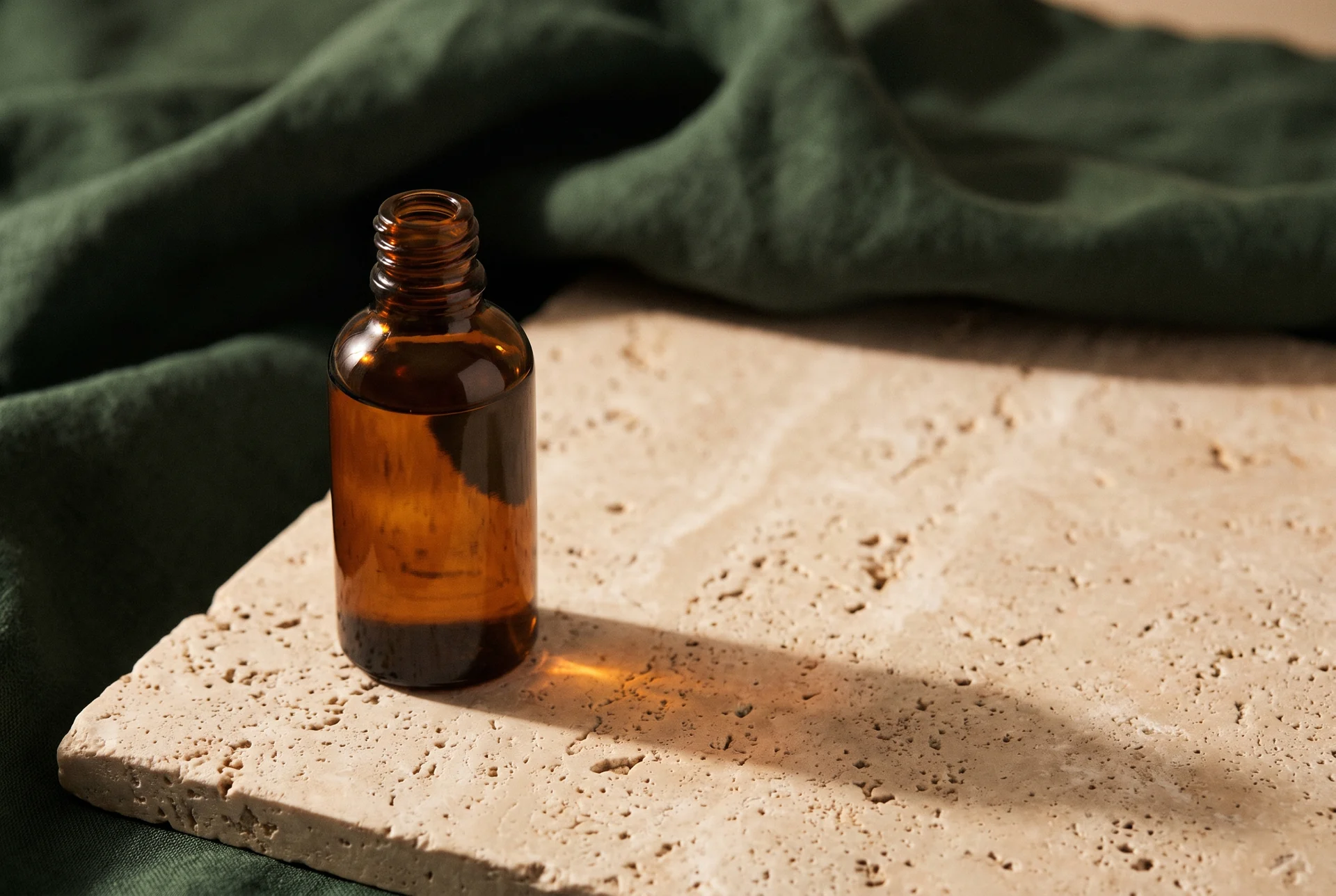 An amber massage-oil bottle on a stone tray over dark green linen.